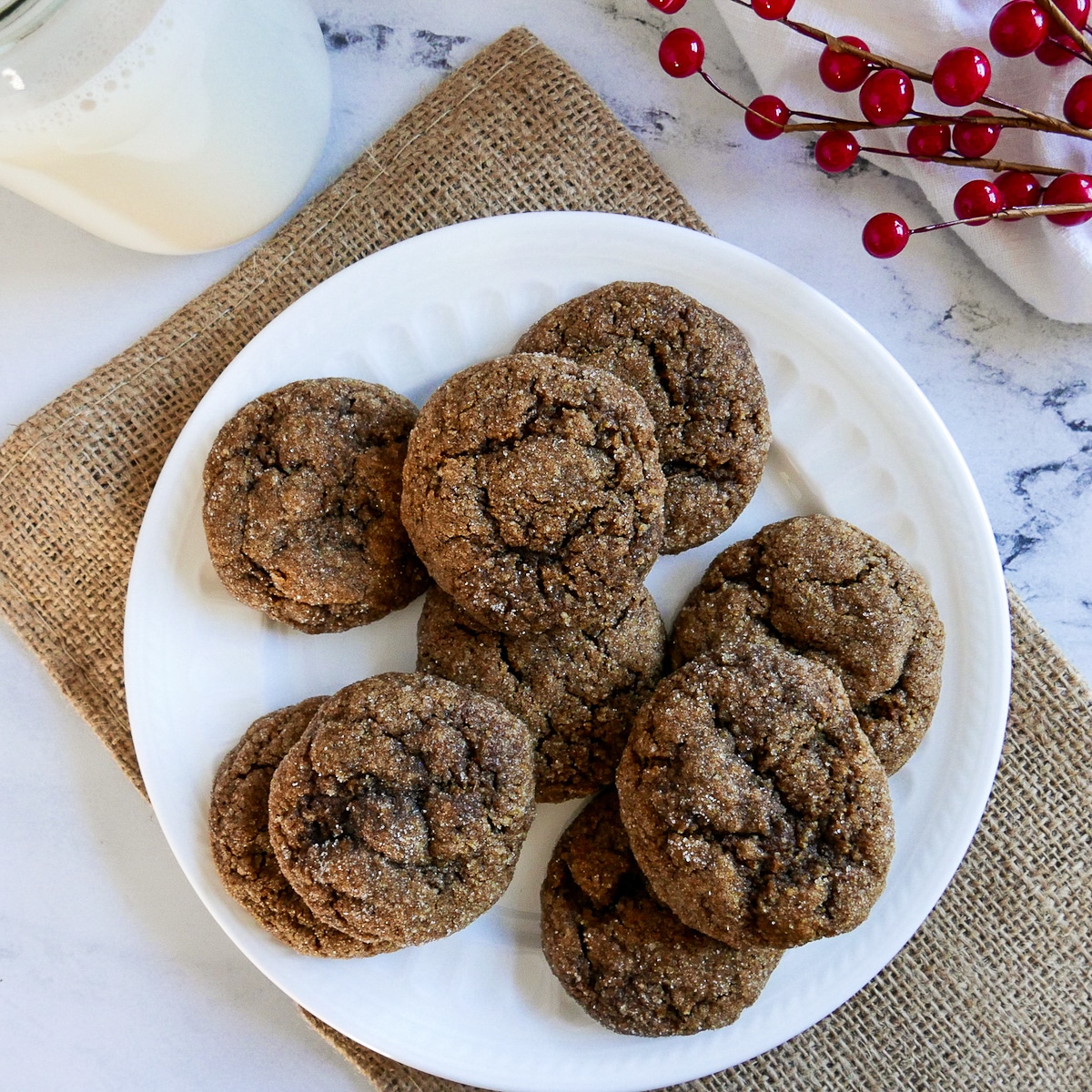 ginger snap cookies on a white plate with glass of milk and holly berries.