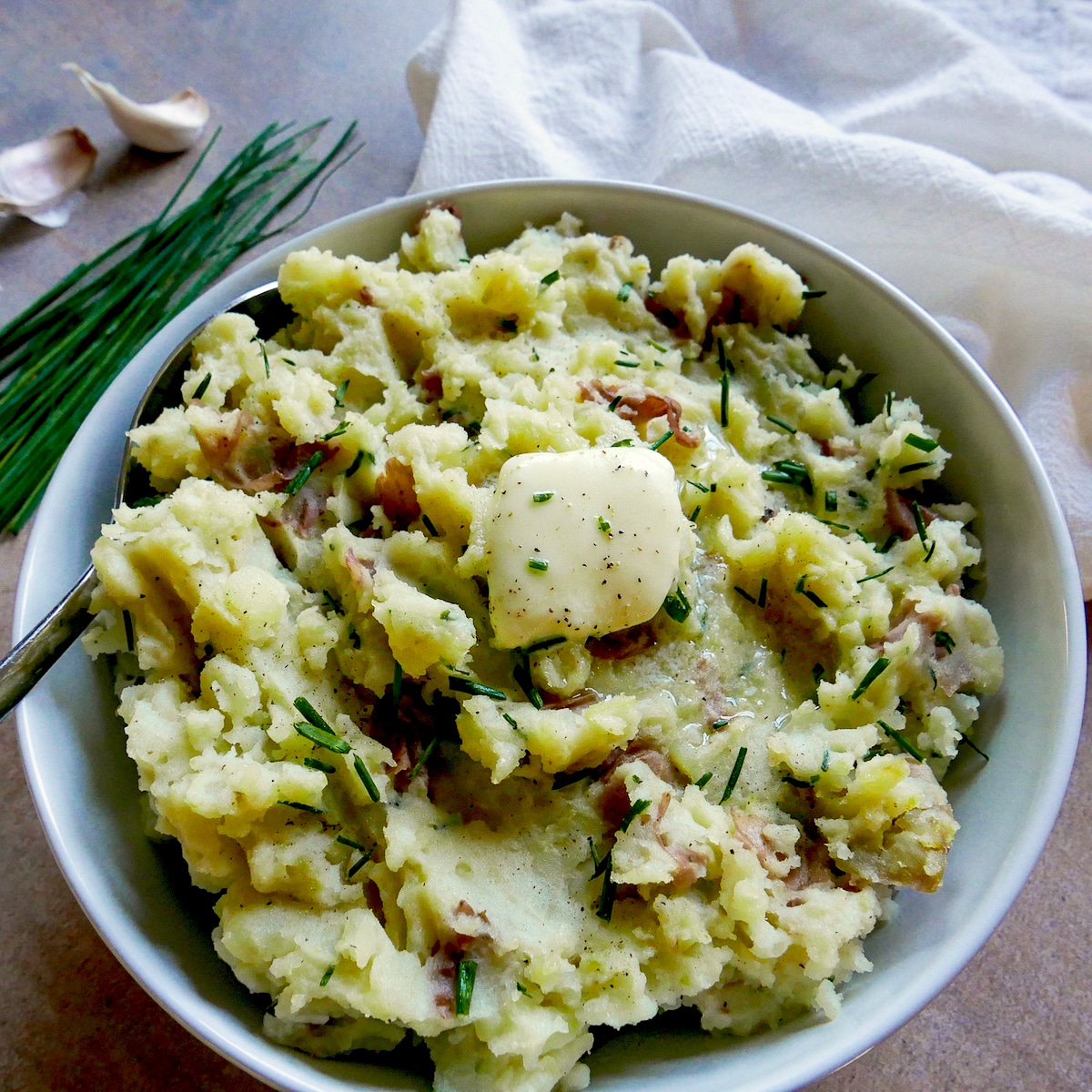 bowl of mashed red potatoes with chives and a white napkin.
