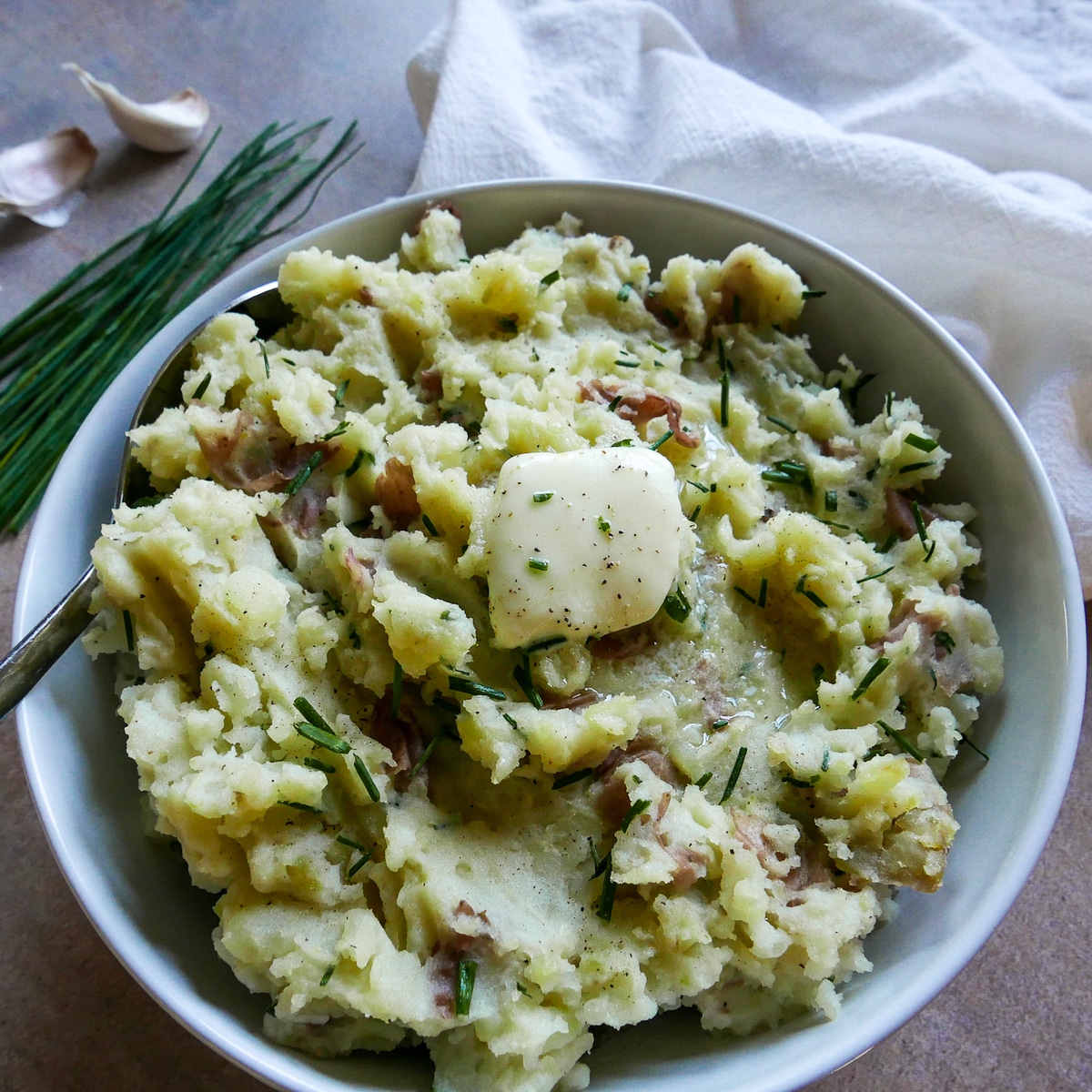red-skin-mashed-potatoes-with-garlic.jpg Bowl of mashed potatoes with garlic and a pat of butter and spoon.