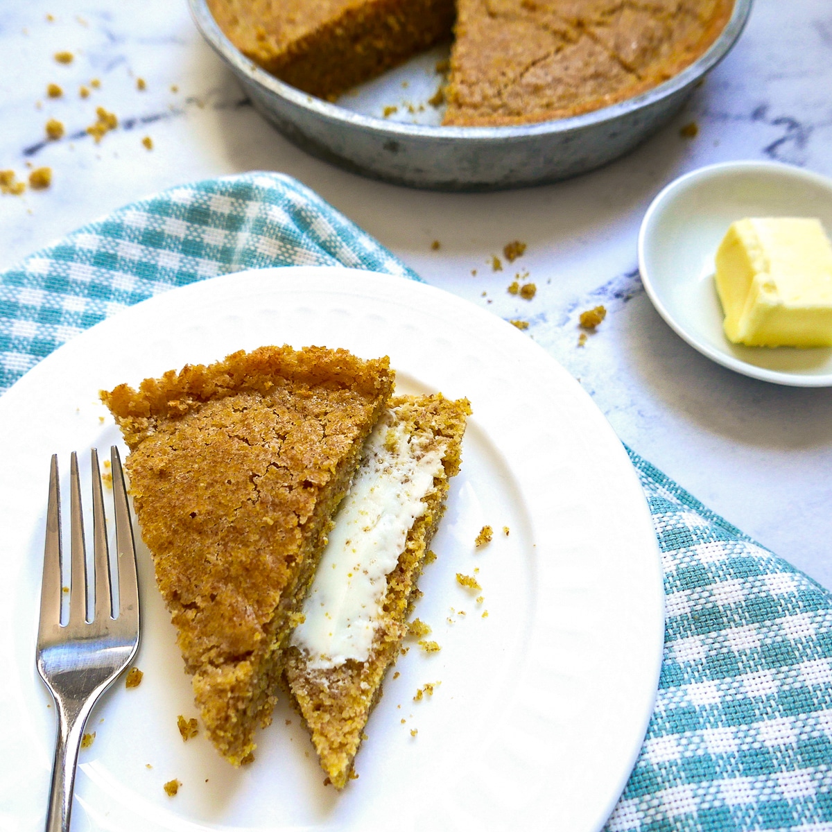 A slice of sourdough cornbread cut in half on a plate with butter and fork.