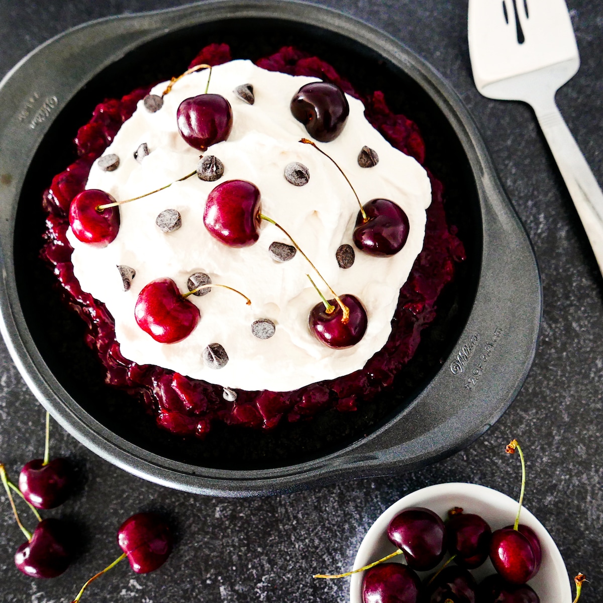 black forest pie with pie server on the side and cup of cherries on table.