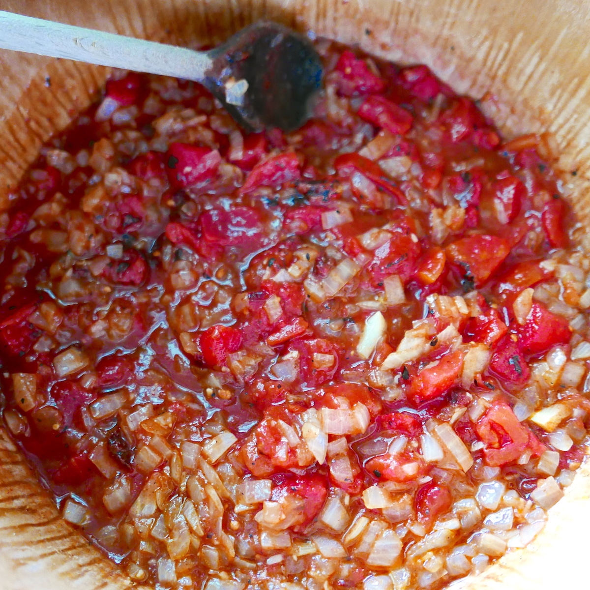 Soup ingredients being stirred in a large pot with a wooden spoon.