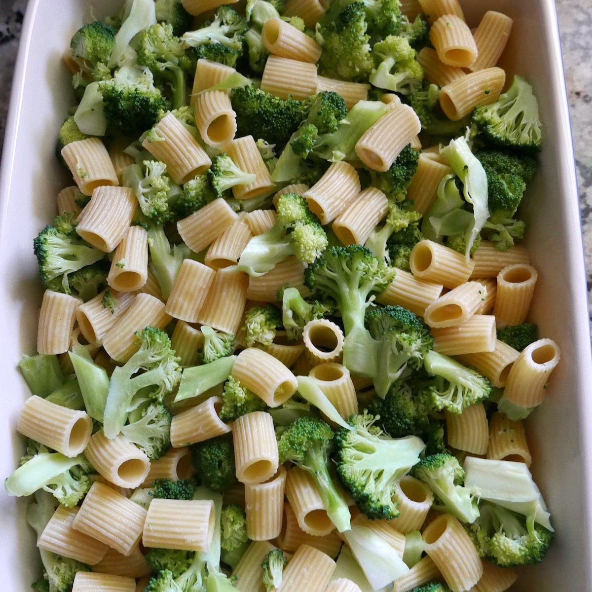 Cooked broccoli and pasta spread into a baking dish.