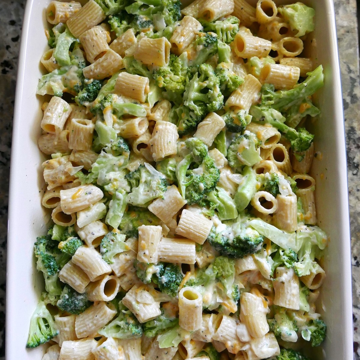 Cheese sauce mixed into pasta and broccoli in a baking dish.