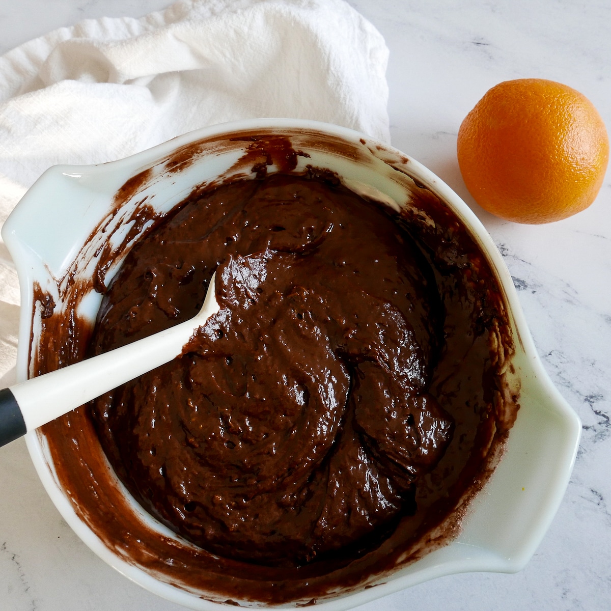 wet ingredients mixed into cake batter with an orange on the side.