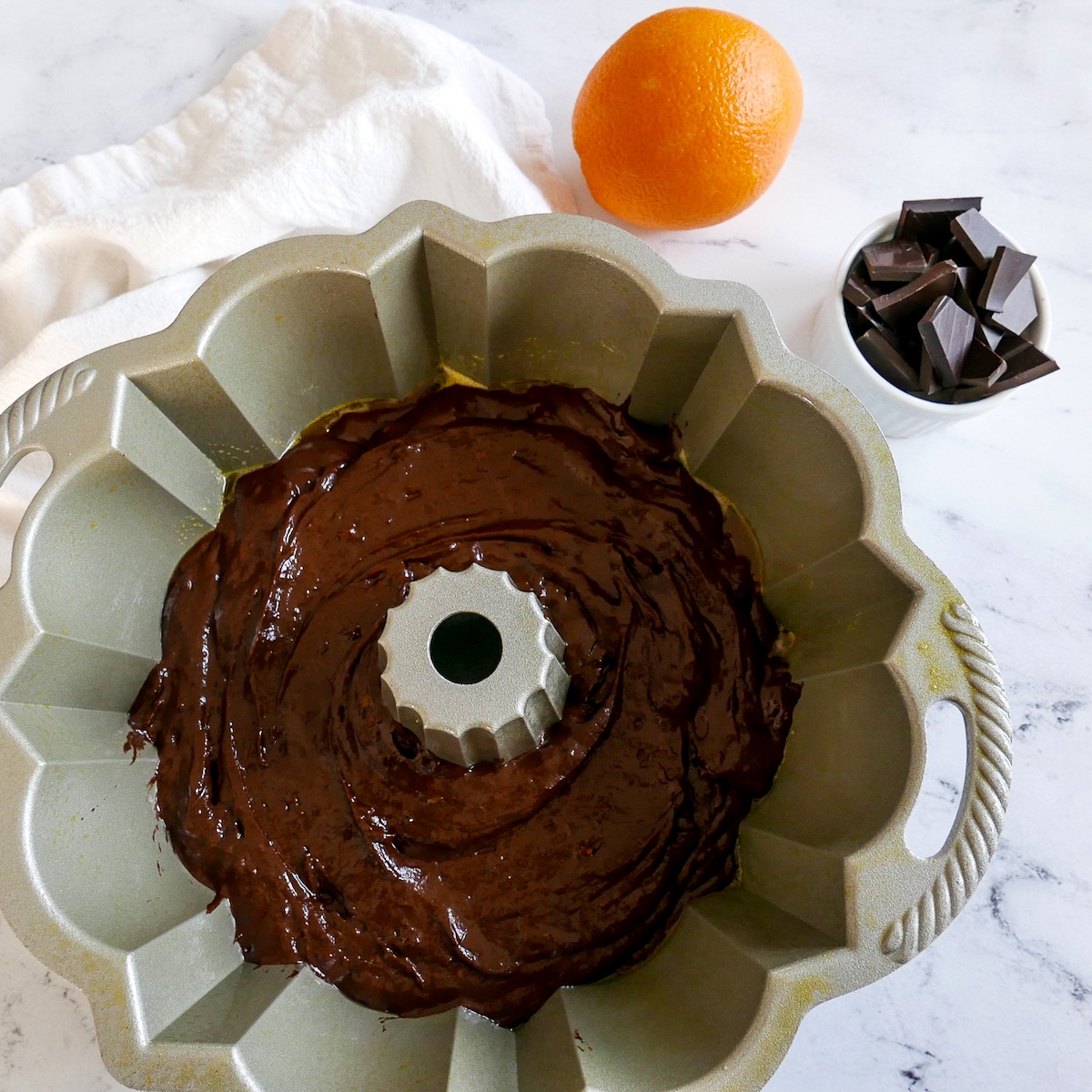 cake batter poured into bundt pan with chopped chocolate and an orange in the background.