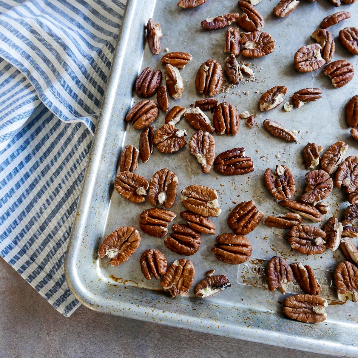 toasted pecans on a baking sheet with a blue napkin underneath.