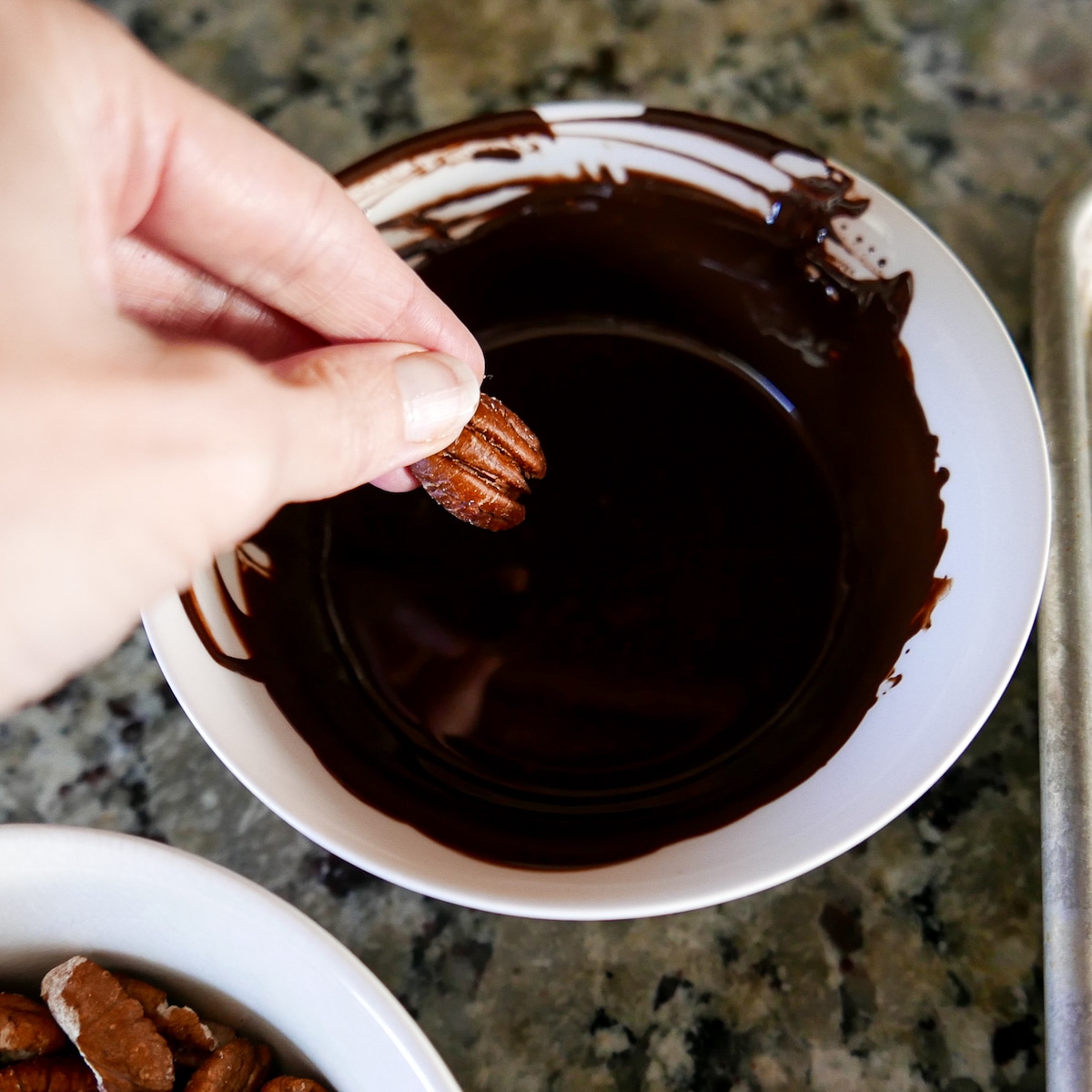 hand dipping toasted pecan into bowl of dark chocolate.