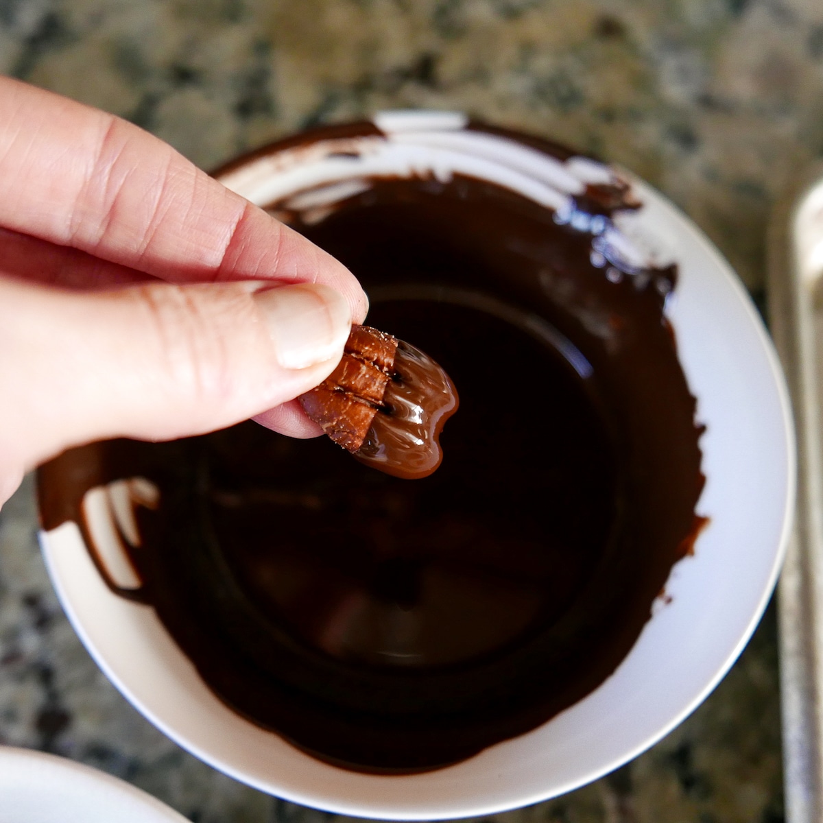 hand holding up chocolate covered pecan from melted bowl of chocolate.