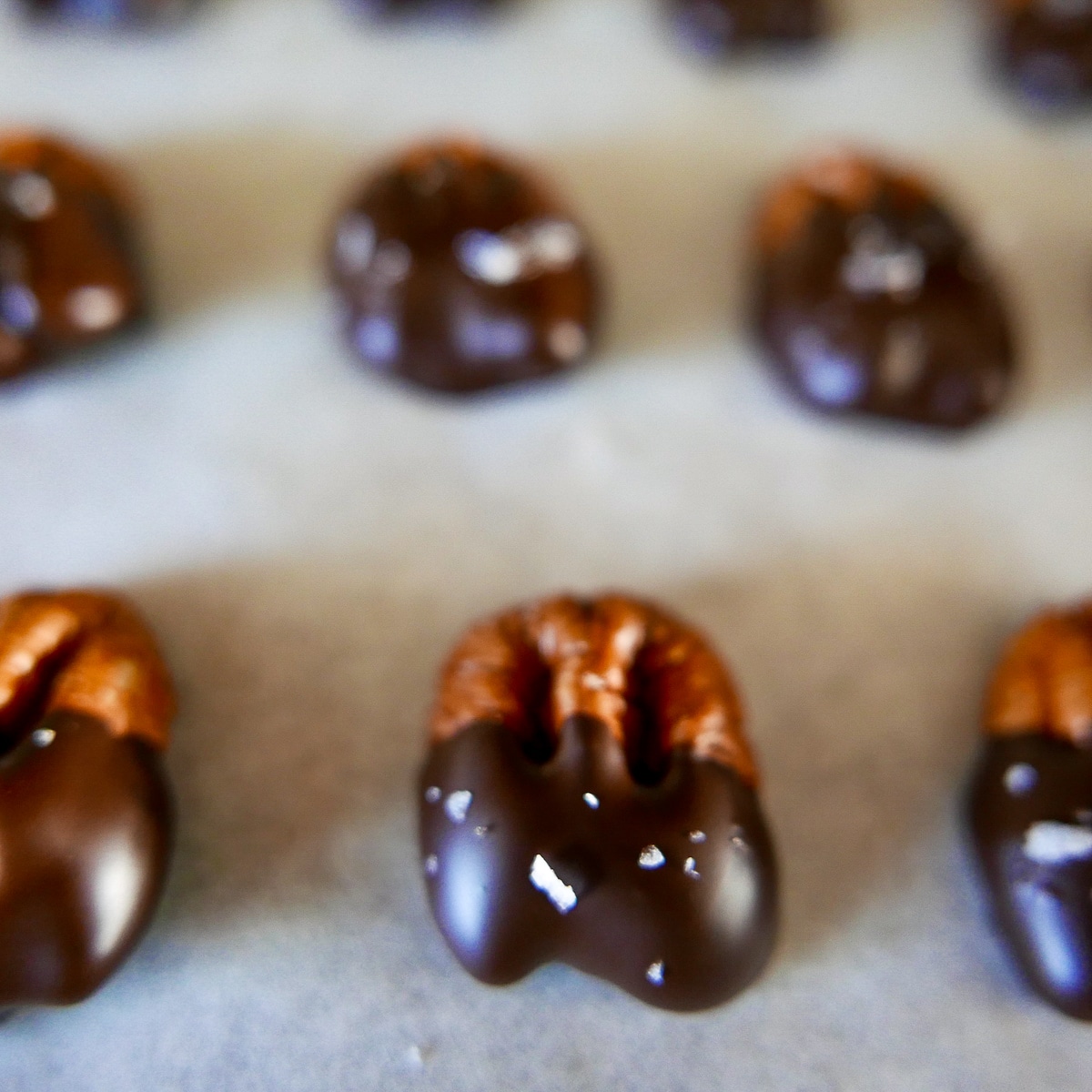 Chocolate dipped pecans setting up on a baking sheet.