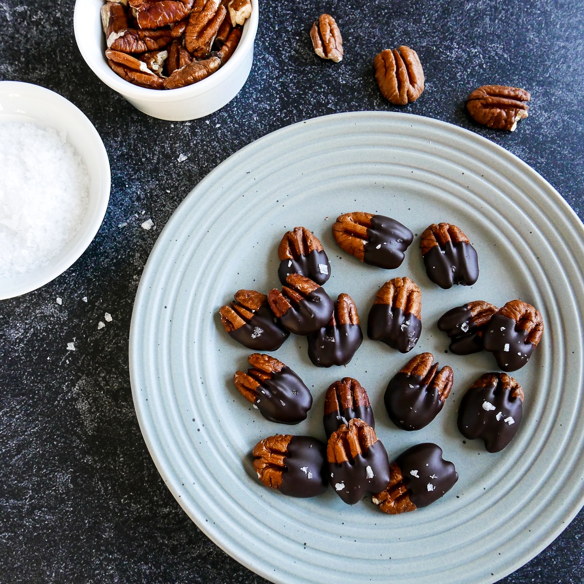 Chocolate dipped pecans arranged on a blue plate with pecans scattered around.