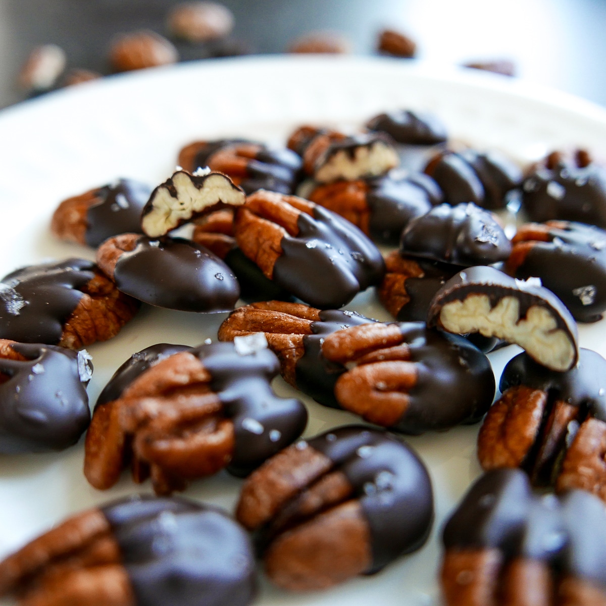 Chocolate covered pecans broken in half and arranged on a white plate.