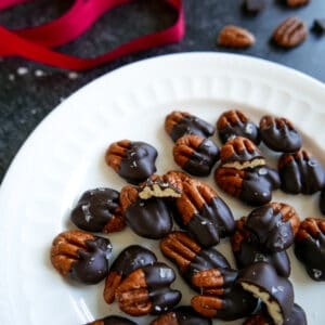 chocolate covered pecans on a white plate with red ribbon in background.