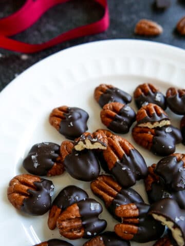 chocolate covered pecans on a white plate with red ribbon in background.