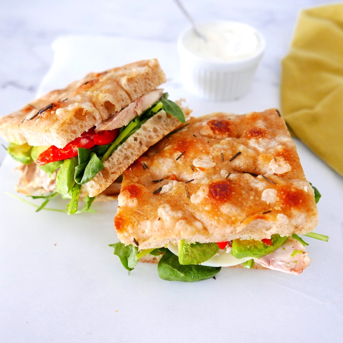 Focaccia sandwich on a plate with cup of mayo in background.