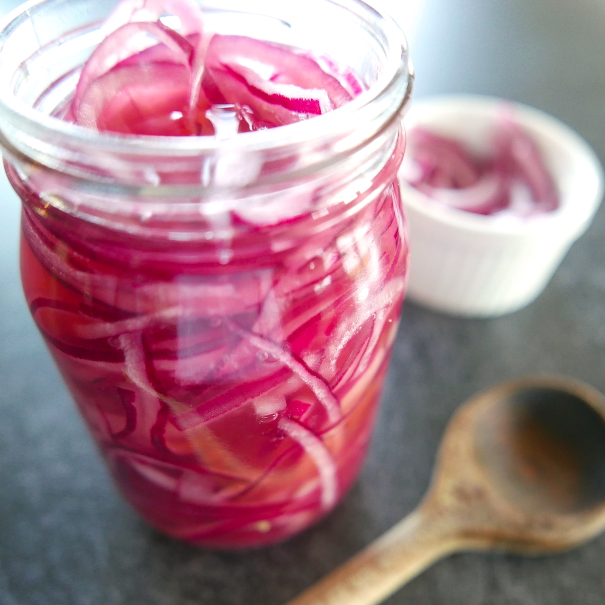 pickled-red-onions-in-a-jar.jpg pickled red onions in a glass jar with a wooden spoon.