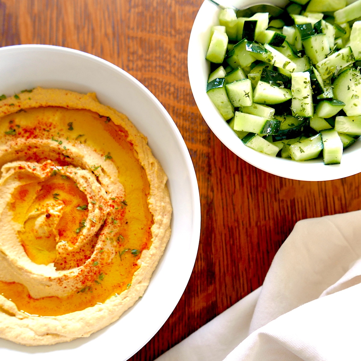 bowl of smoked paprika hummus with cucumber salad next to it.