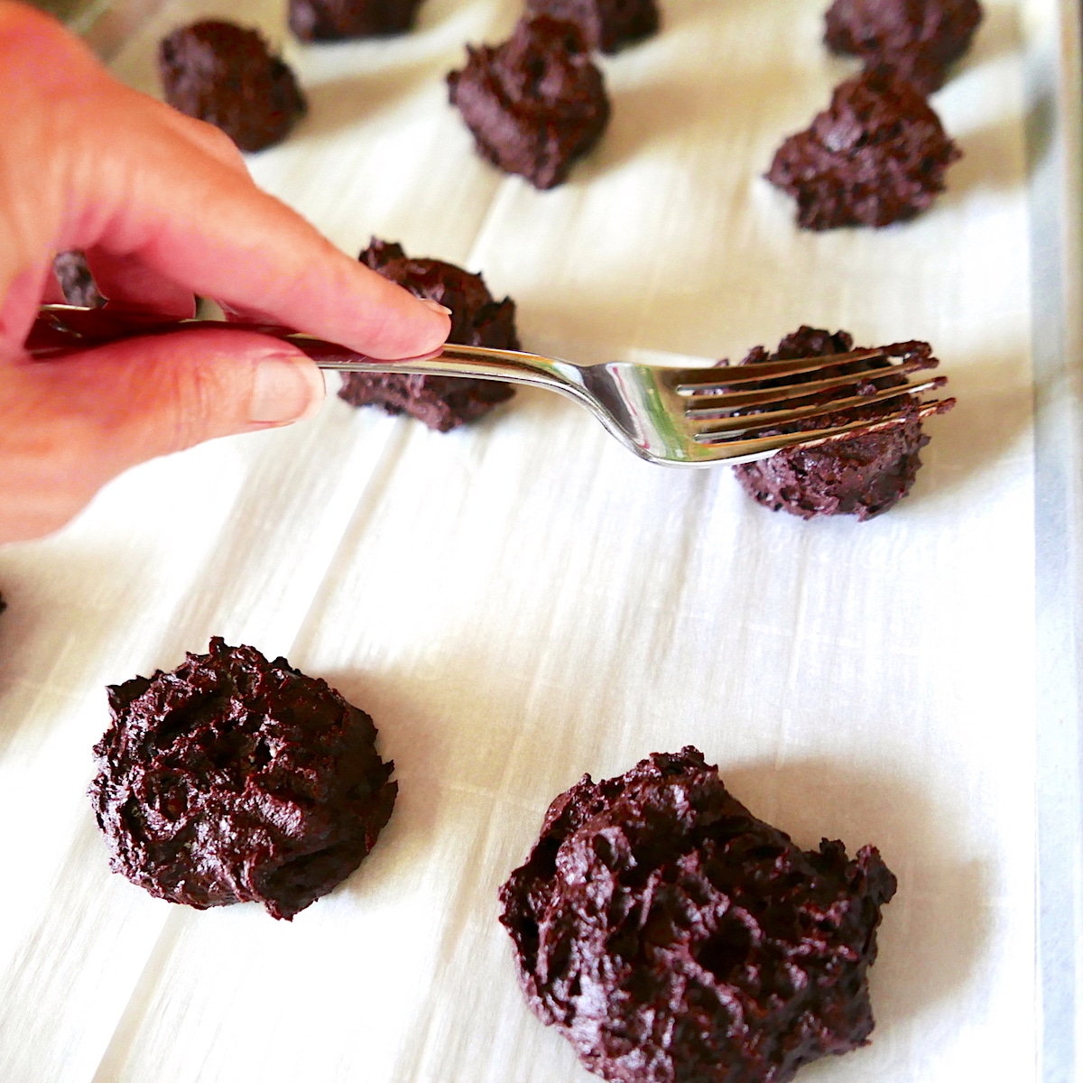 hand pressing fork onto cookies on baking sheet.