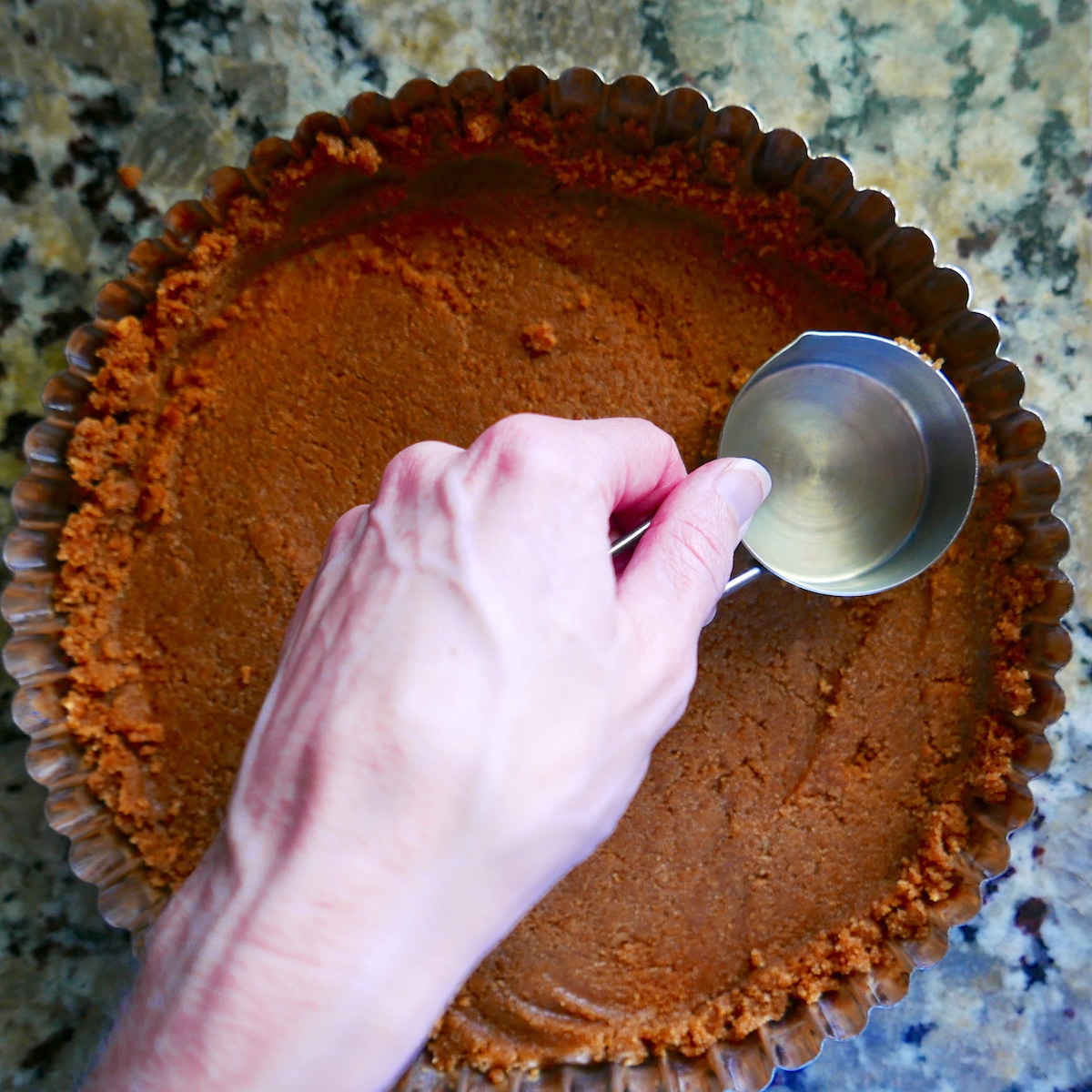 White hand pressing graham cracker crust into tart pan.