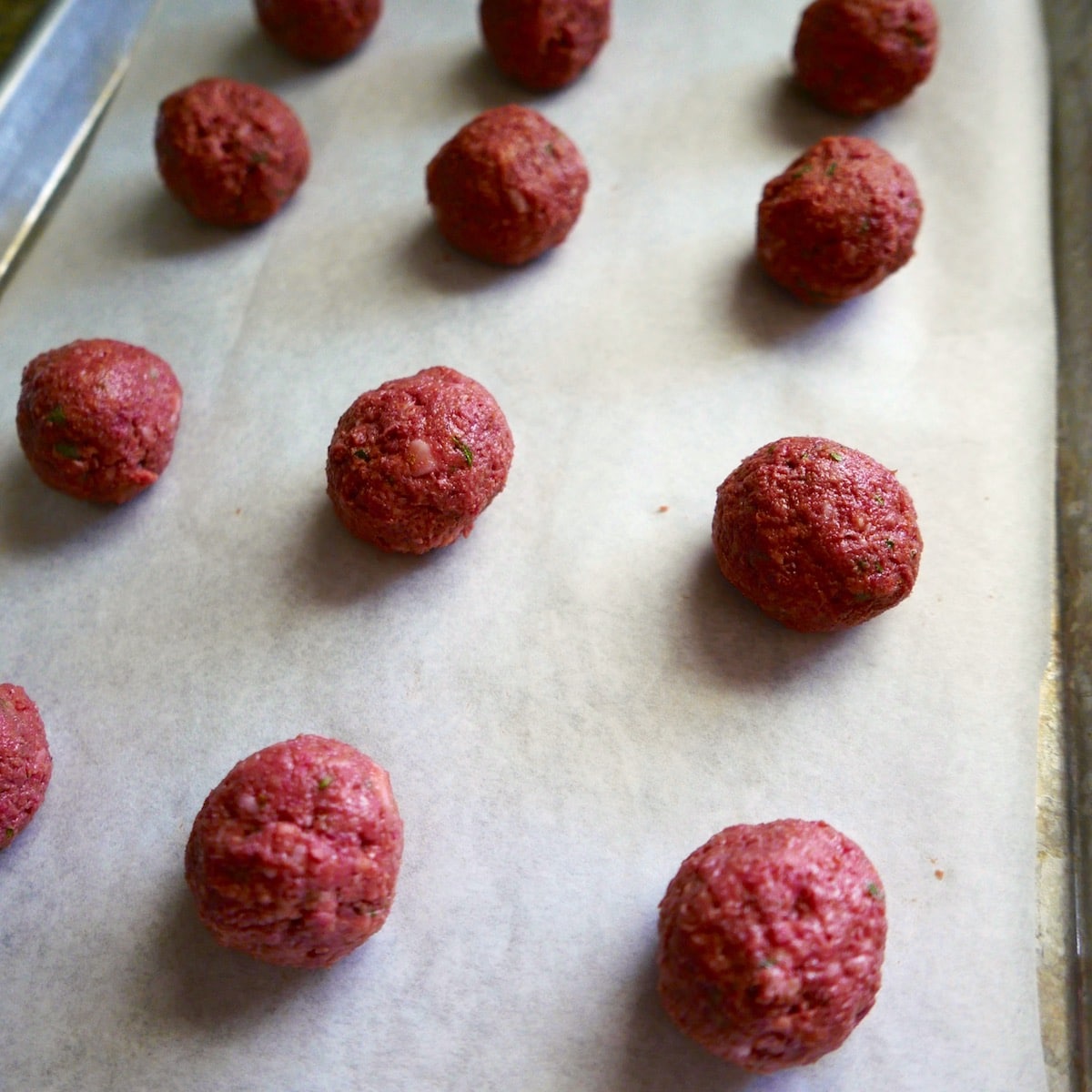 Prepped meatballs arranged on a baking sheet.