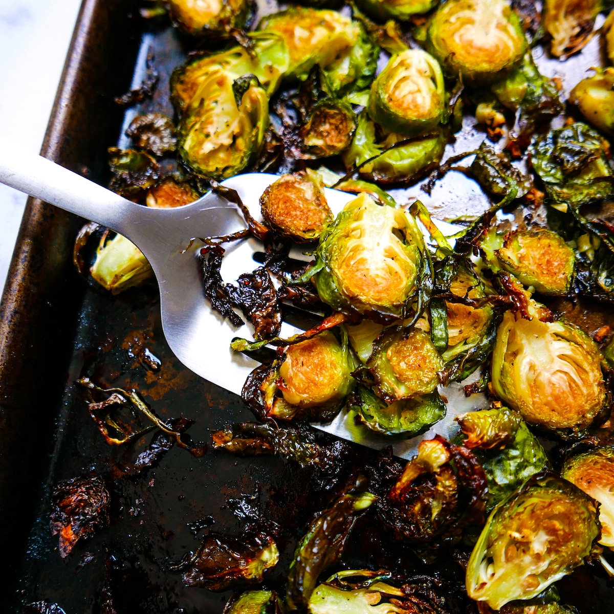 Roasted brussels sprouts being scooped up with a spatula from baking sheet.