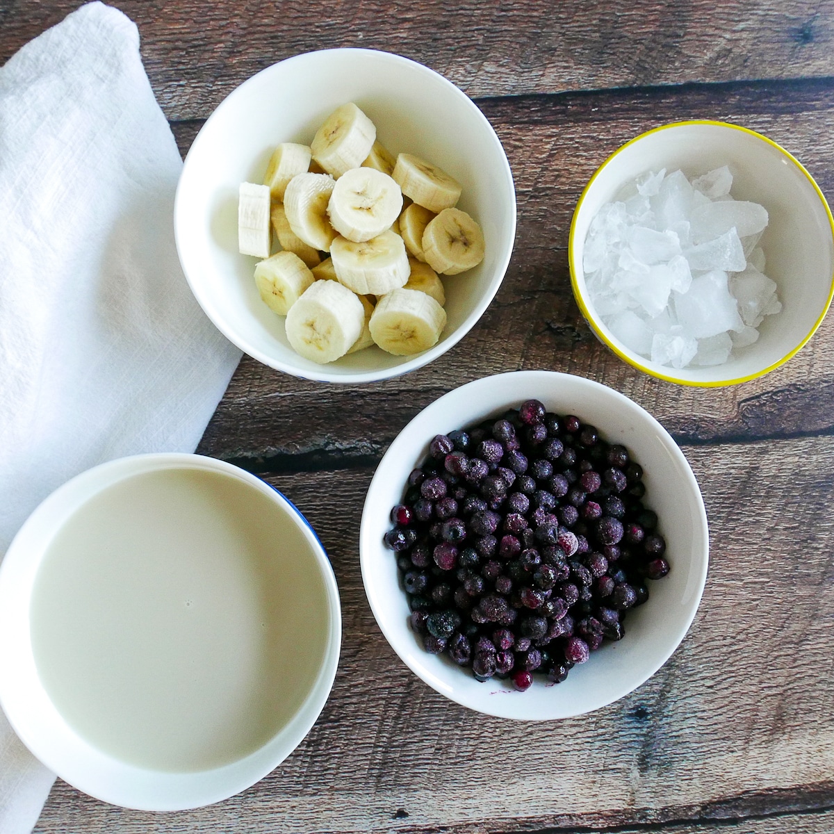 smoothie ingredients arranged in four bowls on a table.