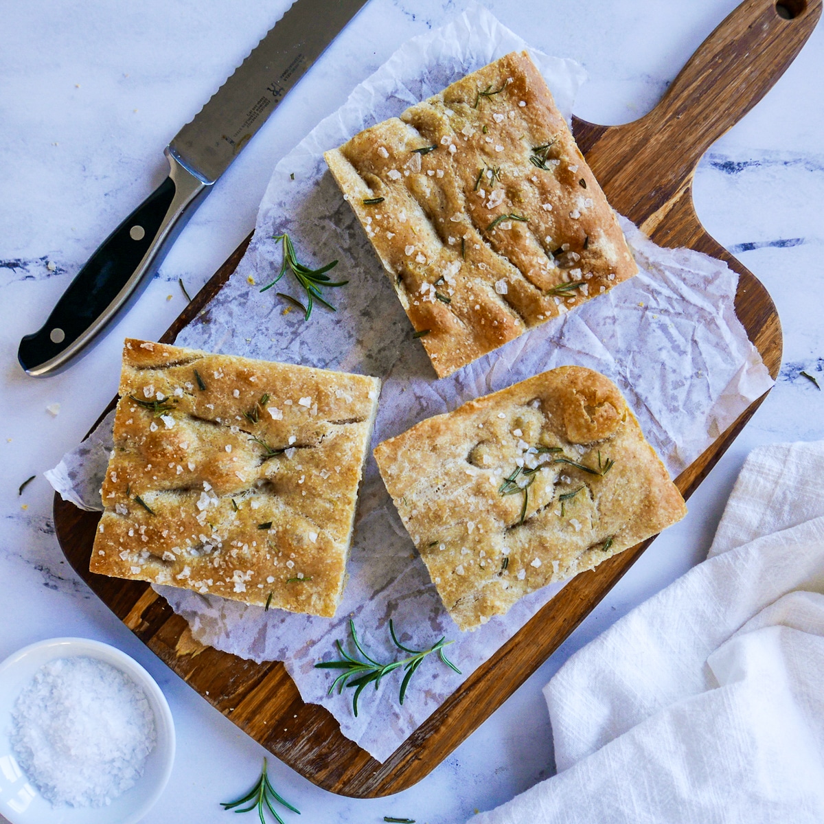 three pieces of focaccia on a wooden cutting board.