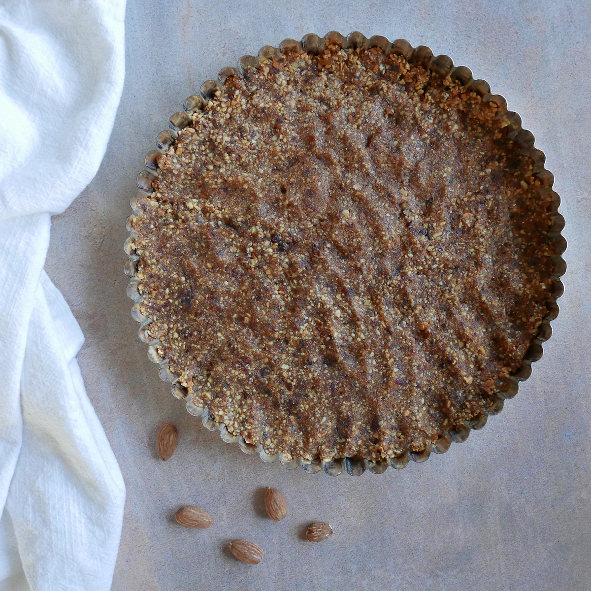 tart crust pressed into tart pan with a few almonds next to it. 
