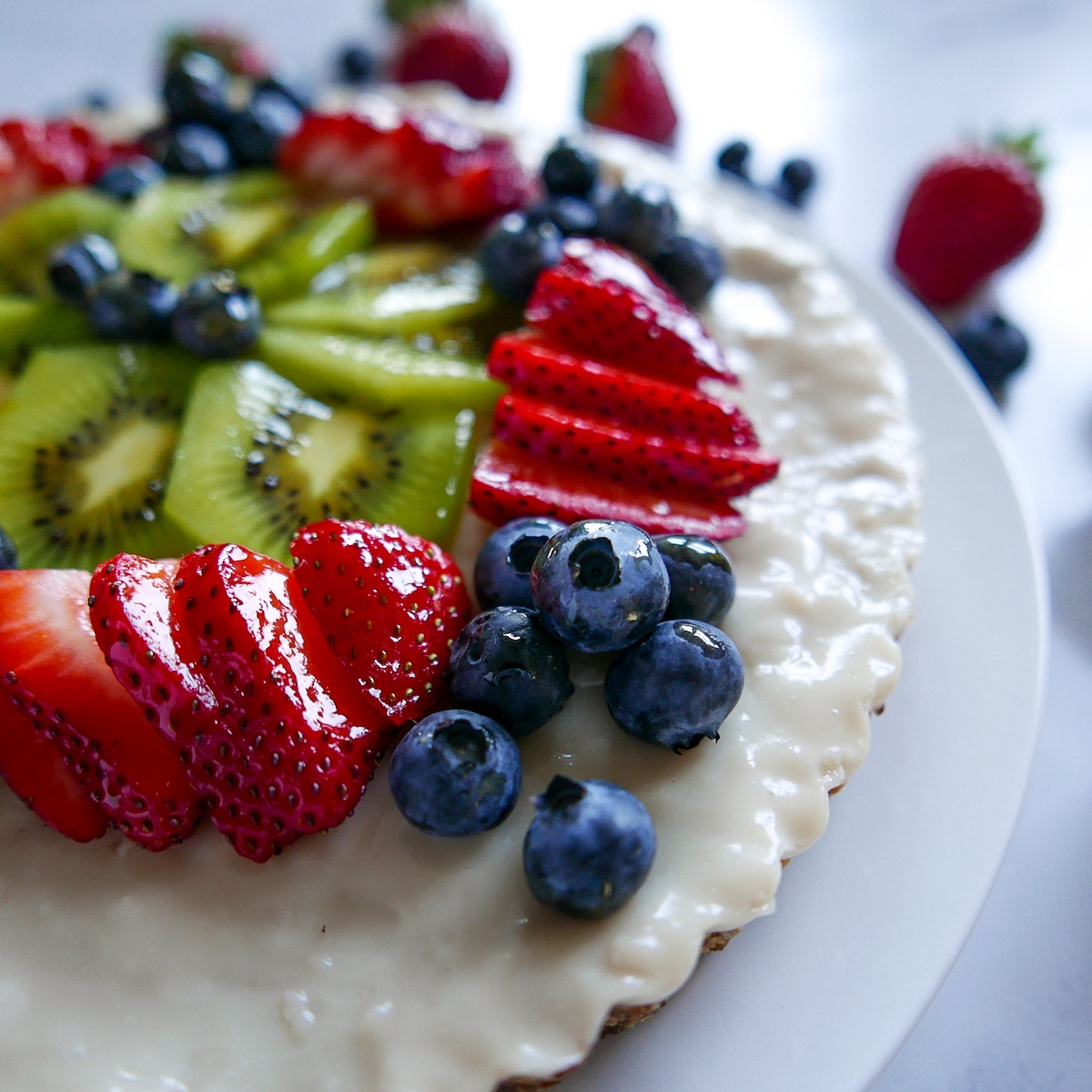Fruit tart topped with berries and kiwi on a white platter with berries.