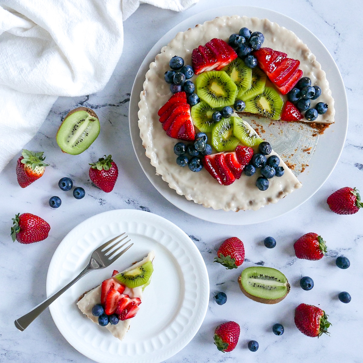 vegan fruit tart on a platter with one slice on a plate and garnished with mixed berries.