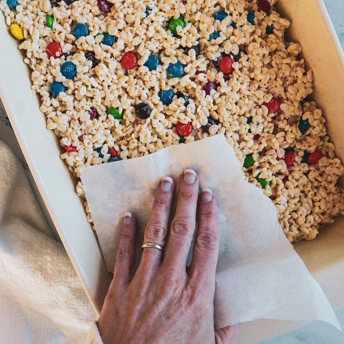 White hand pressing down on pan of rice krispie treats with parchment paper.