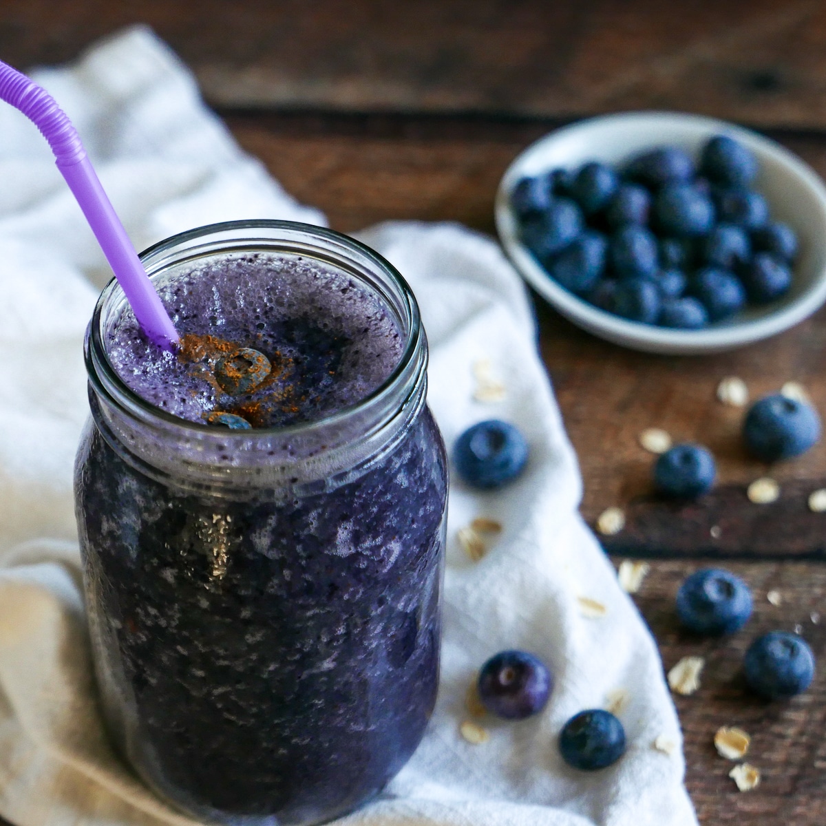 Oat milk protein shake in a glass jar and a cup of blueberries in the background.