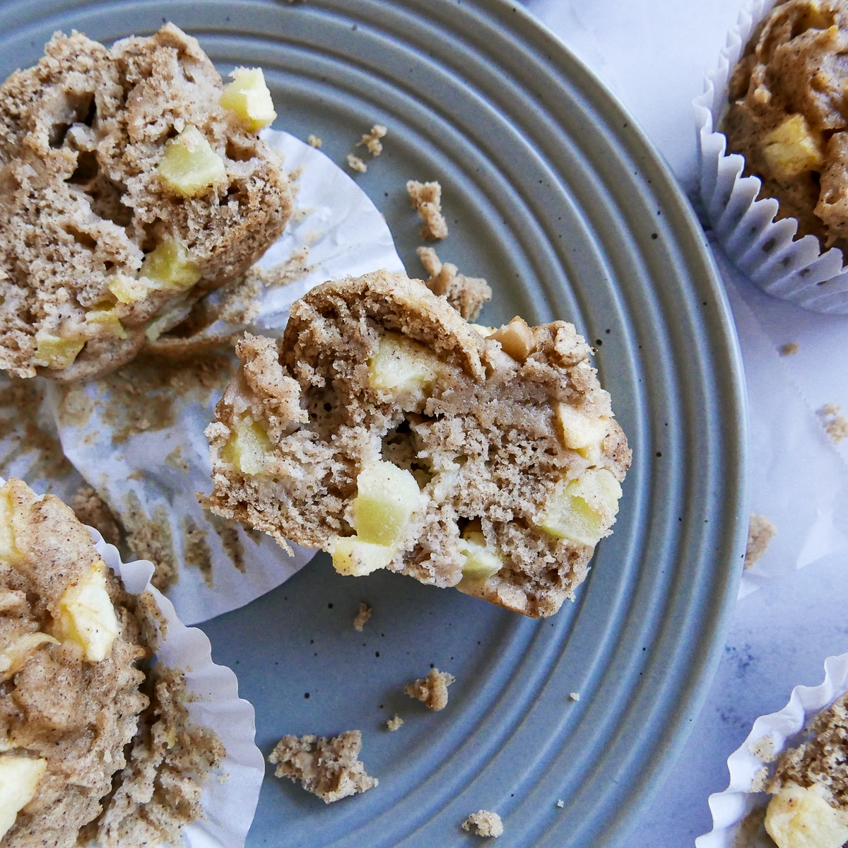 Gluten free apple muffins cut open on a plate with crumbs.