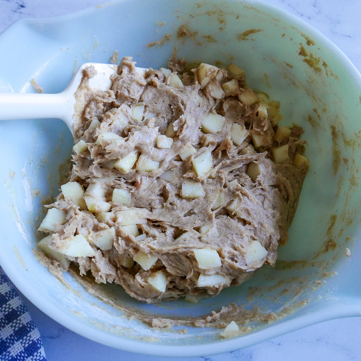 Diced apples being folded into muffin batter with a rubber spatula.