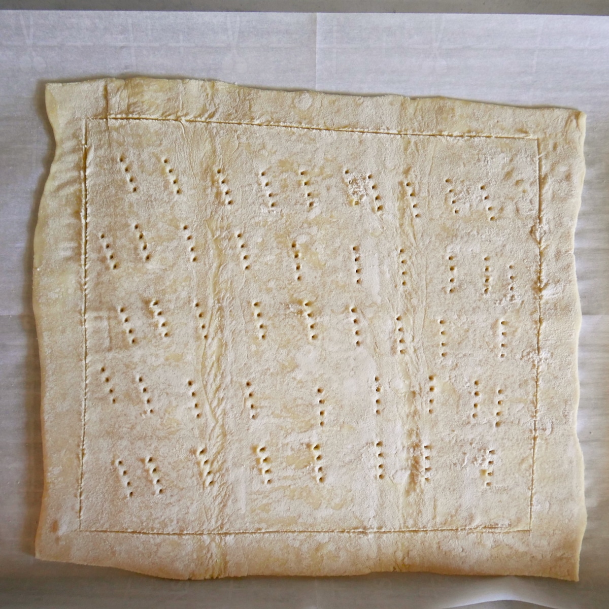 Scored and pierced puff pastry rolled out on parchment paper.