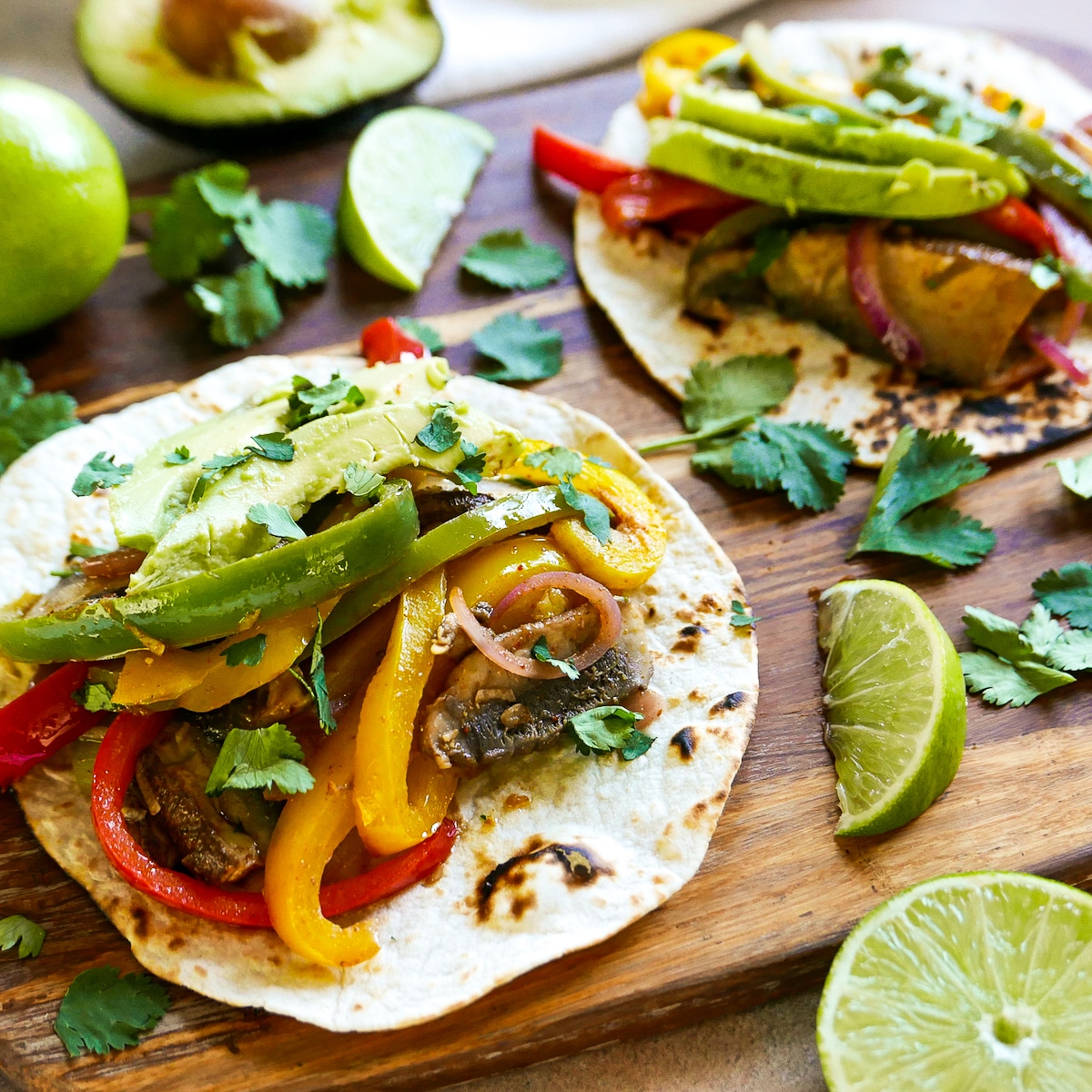 Fajitas arranged on a wooden cutting board with cilantro and sliced limes.