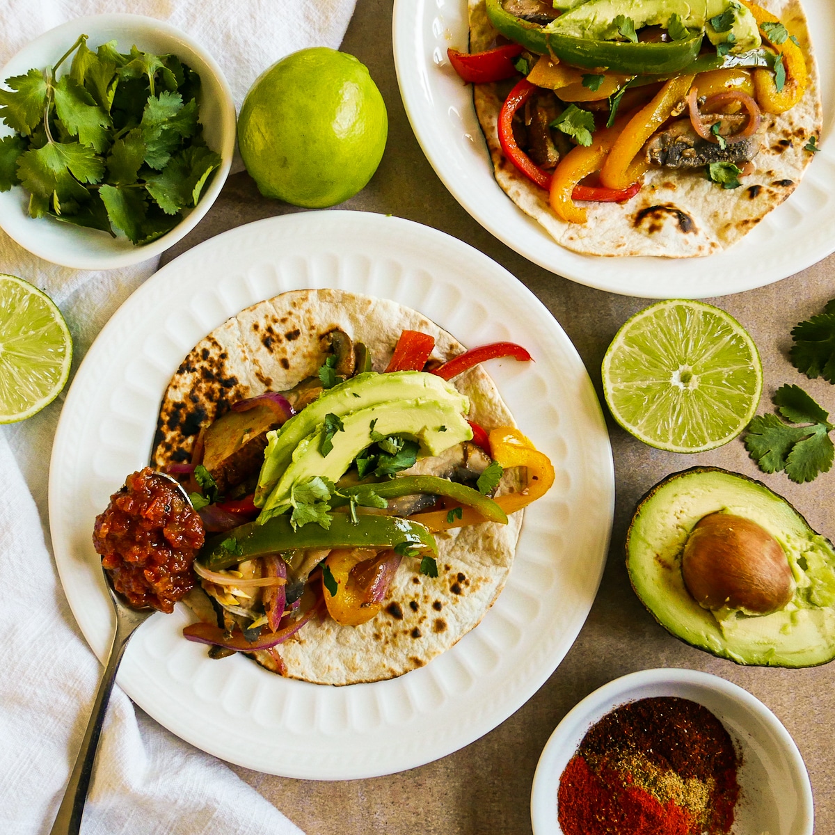 fajitas-with-salsa.jpg Two fajitas on plates with sliced limes and a spoonful of salsa resting on plate.