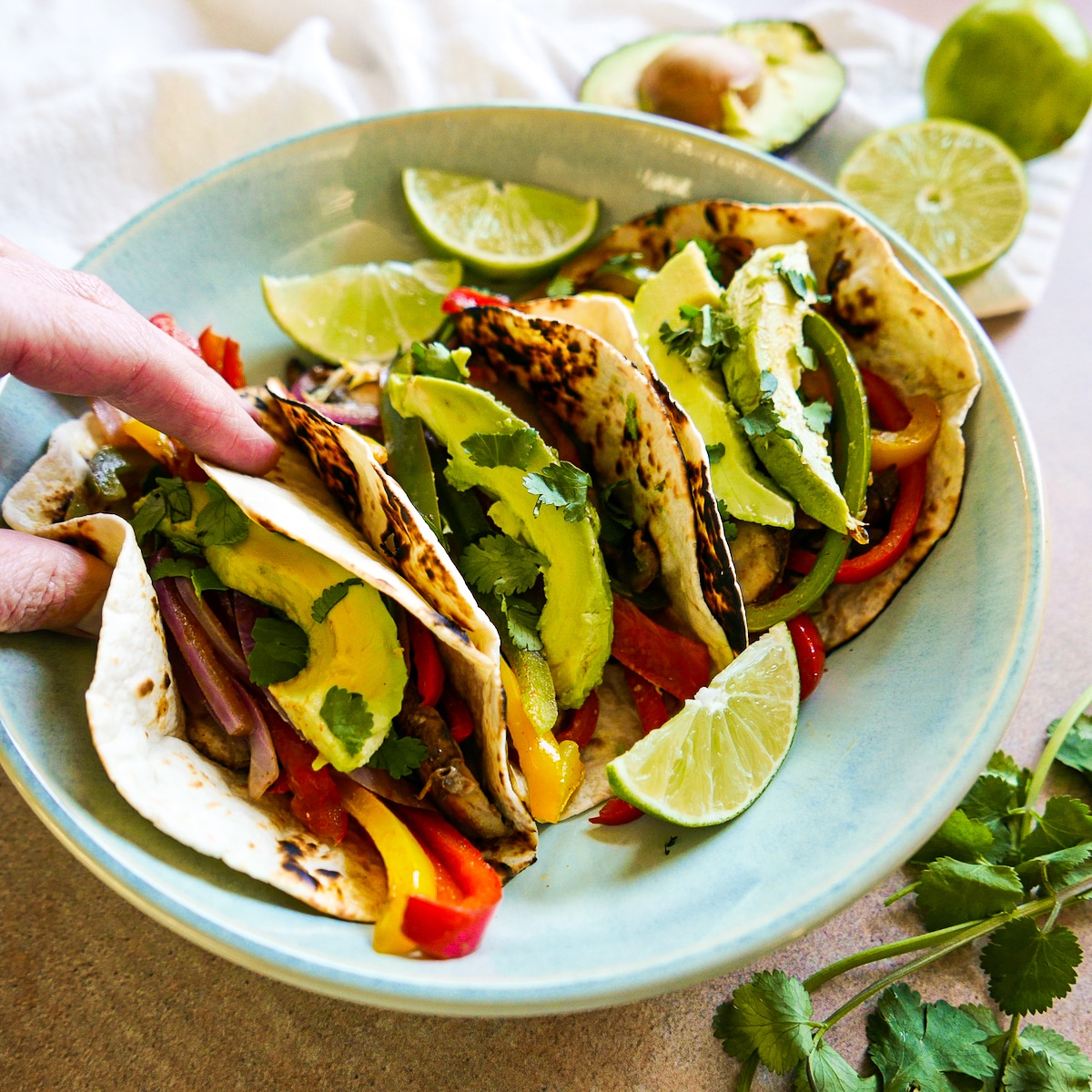 hand-grabbing-fajitas.jpg white hand picking up fajita from blue plate.