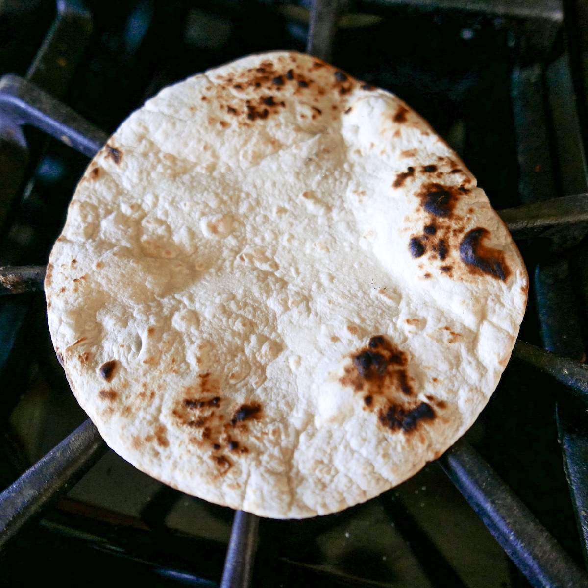 flour tortilla being charred over a gas burner.