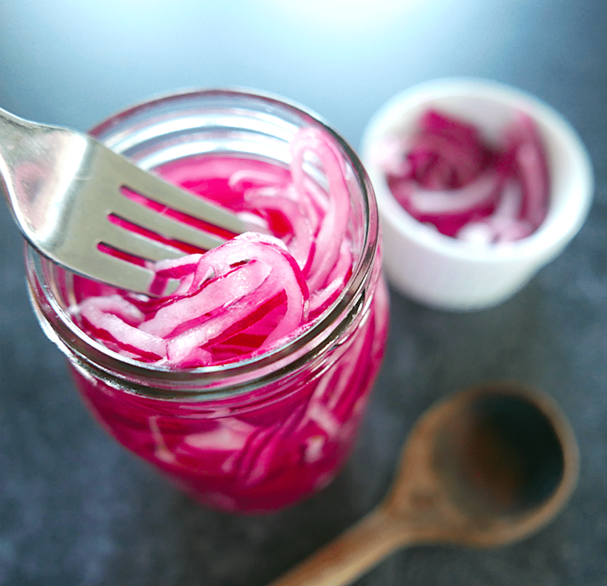 fork dipping into glass jar of quick pickled red onions.