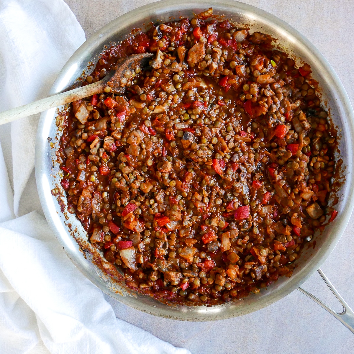 vegan sloppy joe mixture being cooked in a large skillet with a wooden spoon.