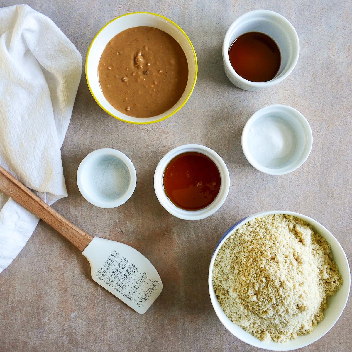 cookie ingredients arranged in bowls with a napkin and rubber spatula.