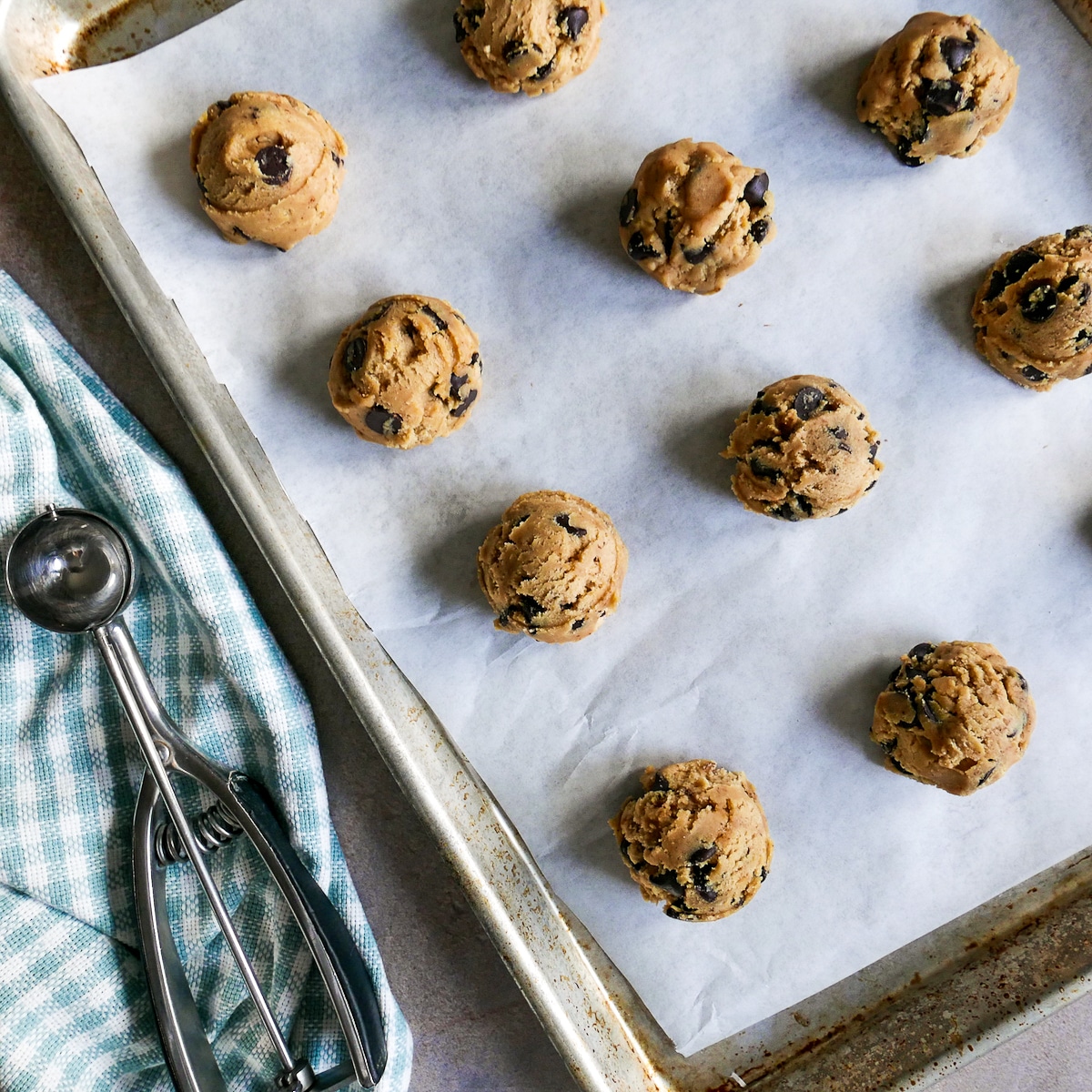 cookie dough portioned out on a baking sheet with a cookie scoop next to sheet.