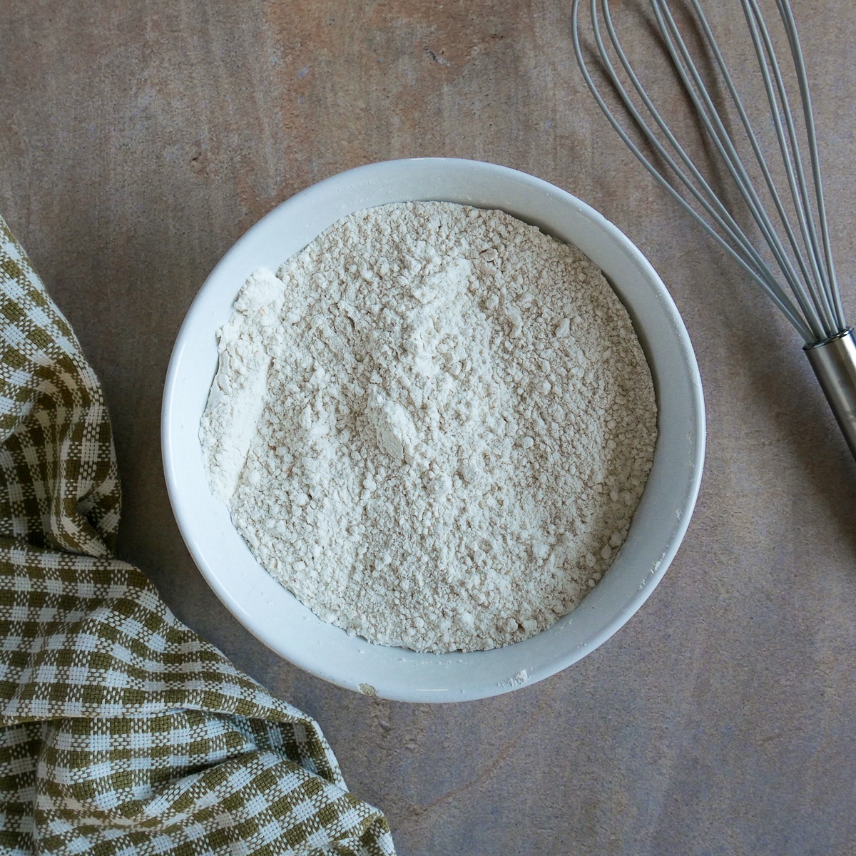 dry ingredients in a mixing bowl with a whisk and napkin next to bowl.