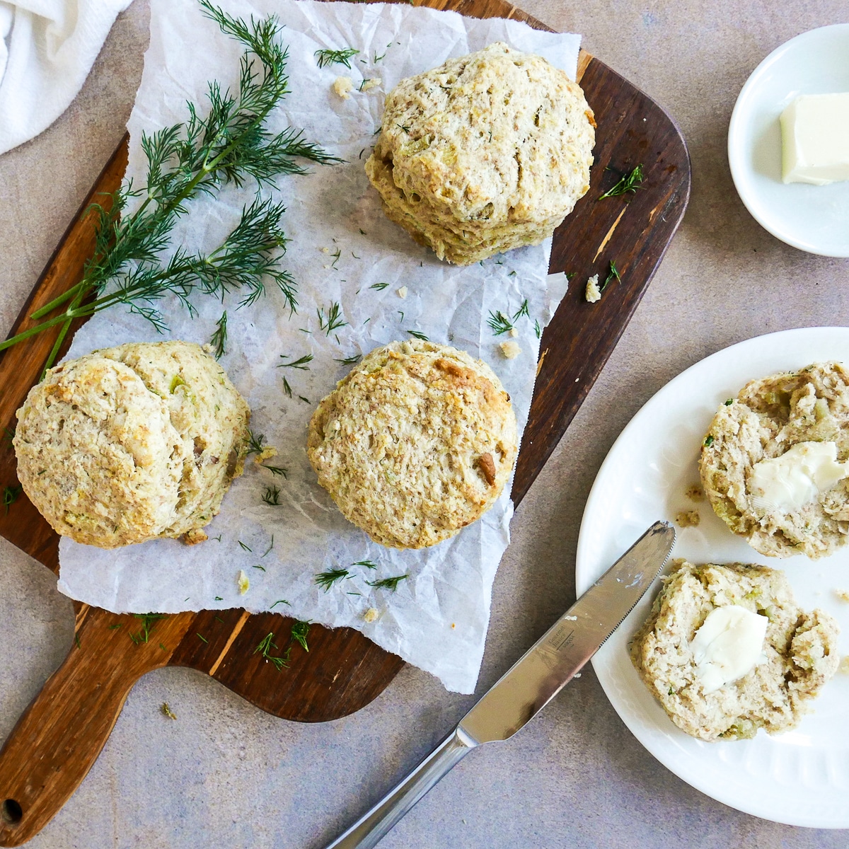 three potato onion dill biscuits on a cutting board with open biscuit on a white plate. 