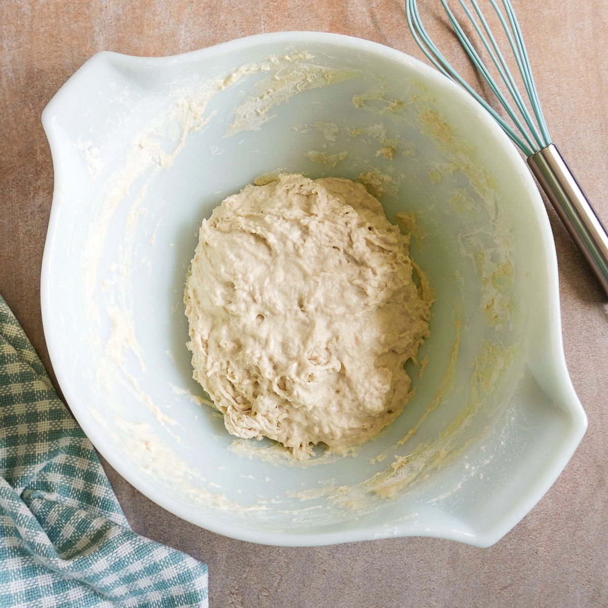 Dough in a mixing bowl with a whisk and napkin.