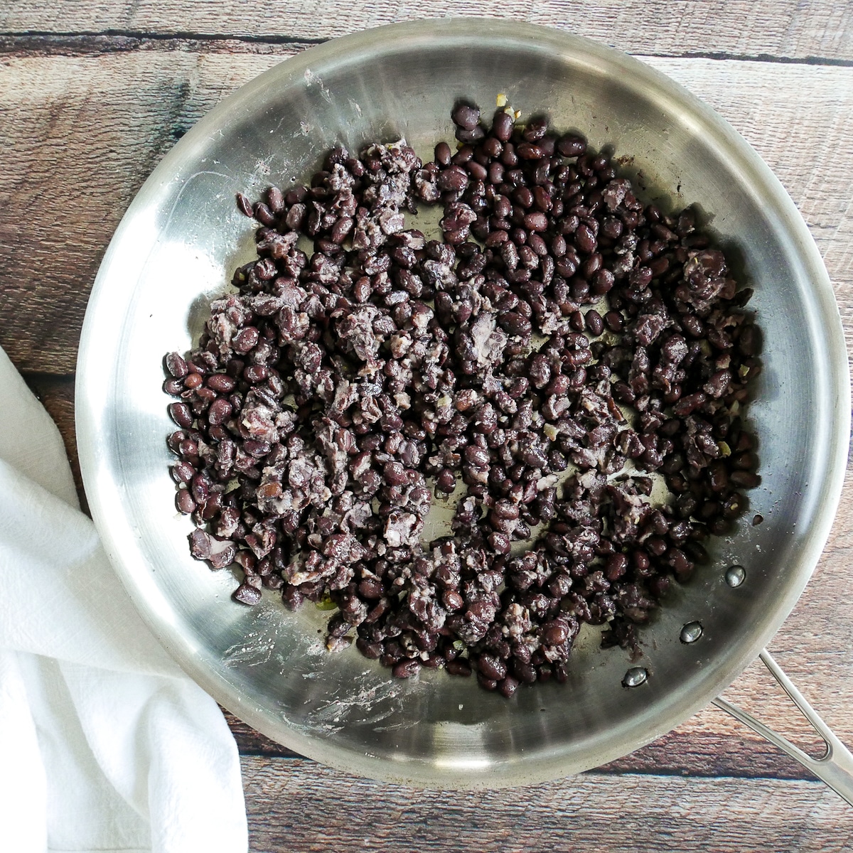 Refried black beans and garlic being cooked in a large skillet.