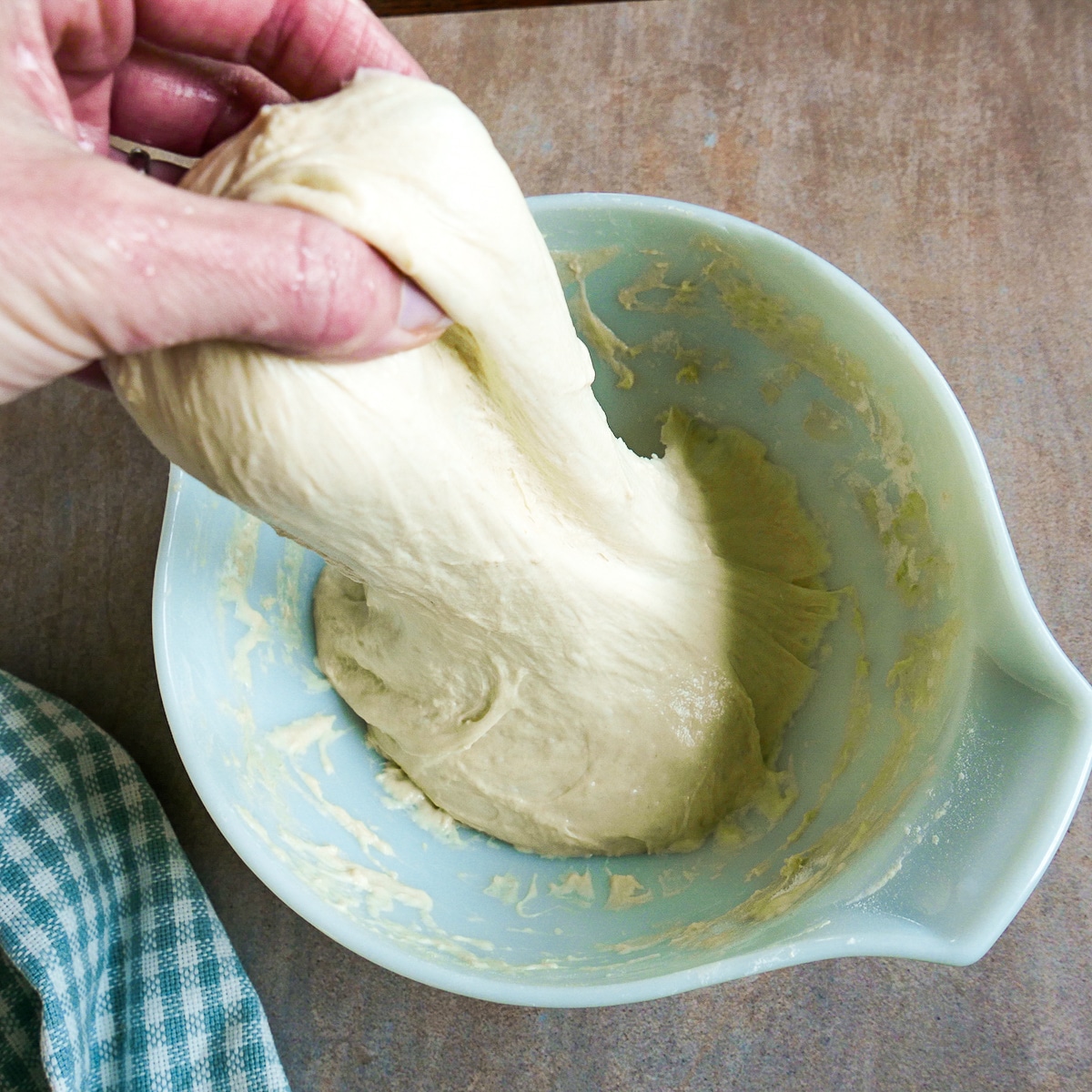 White hand stretching dough in mixing bowl.
