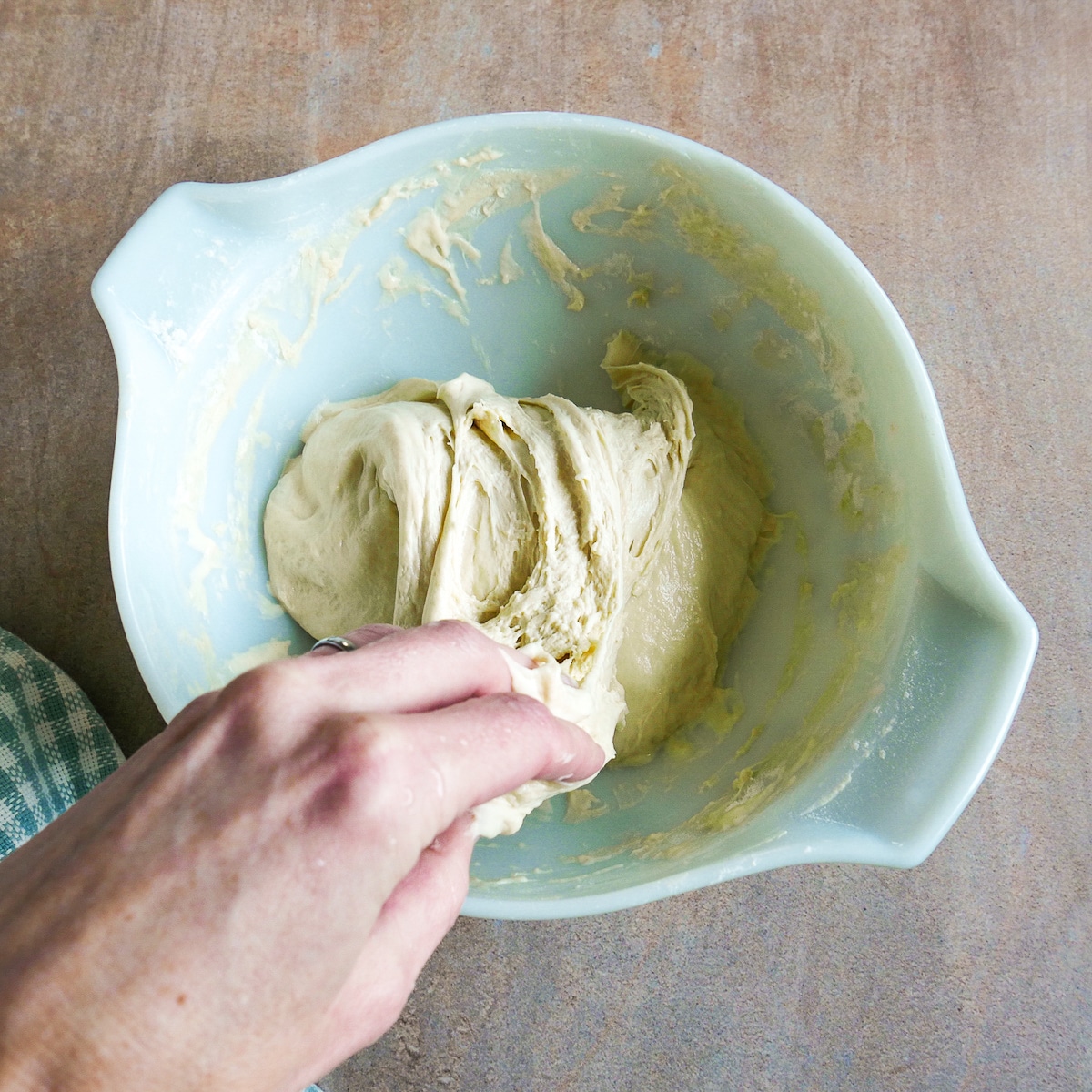 White hand folding dough in mixing bowl.