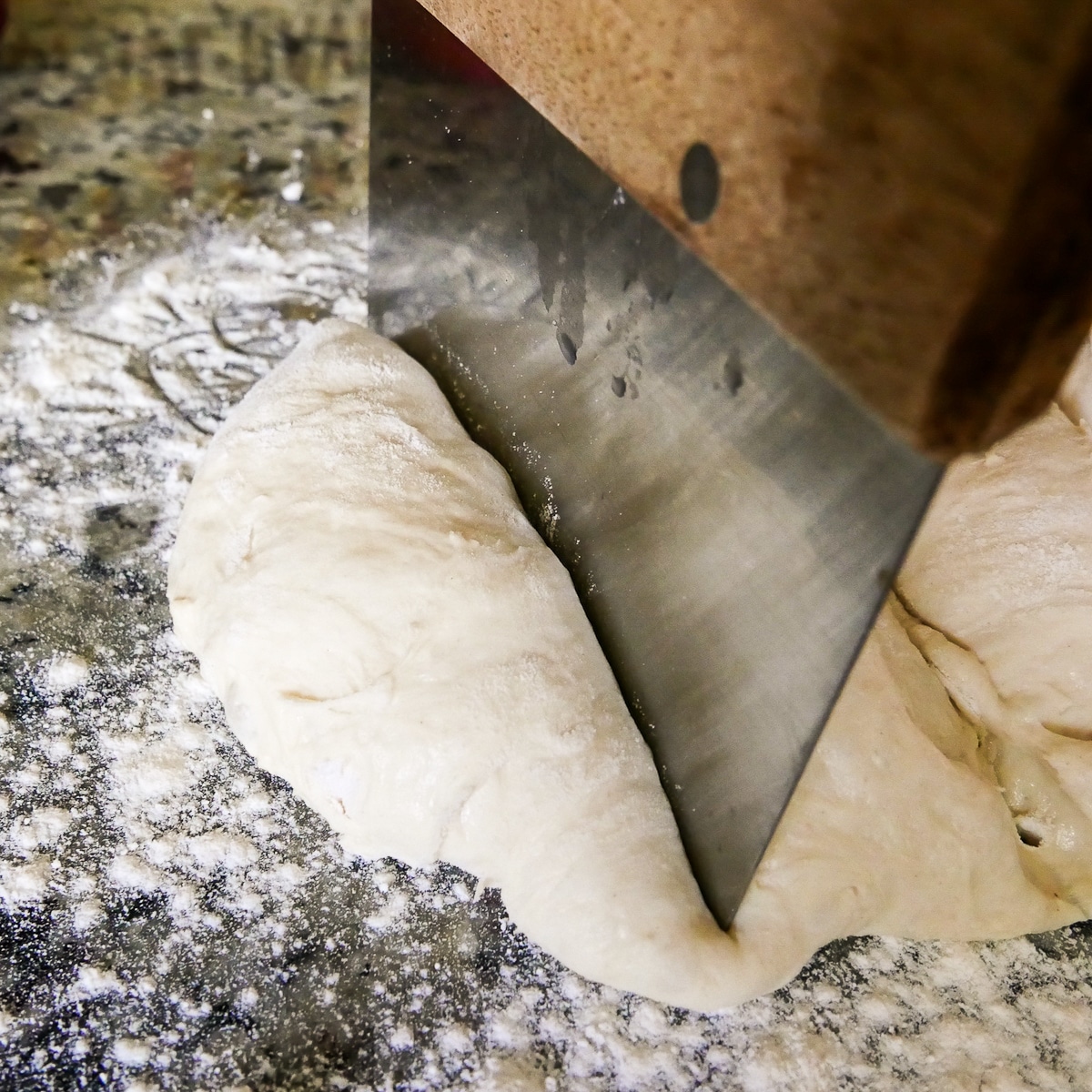 bench scraper cutting dough into four portions.